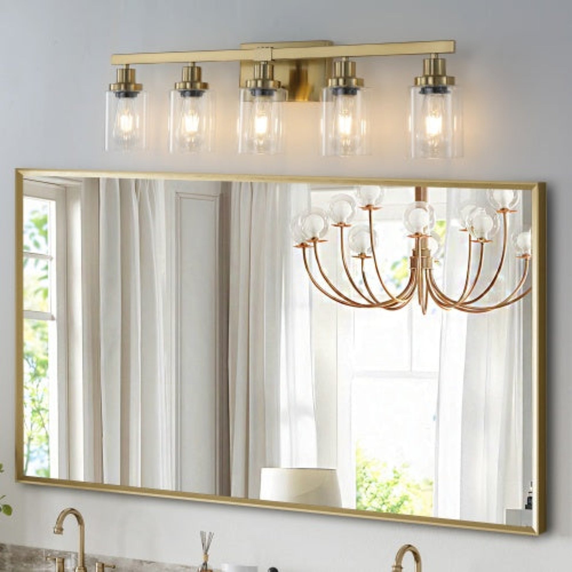 Gold-framed mirror with a chandelier-style light fixture above it
